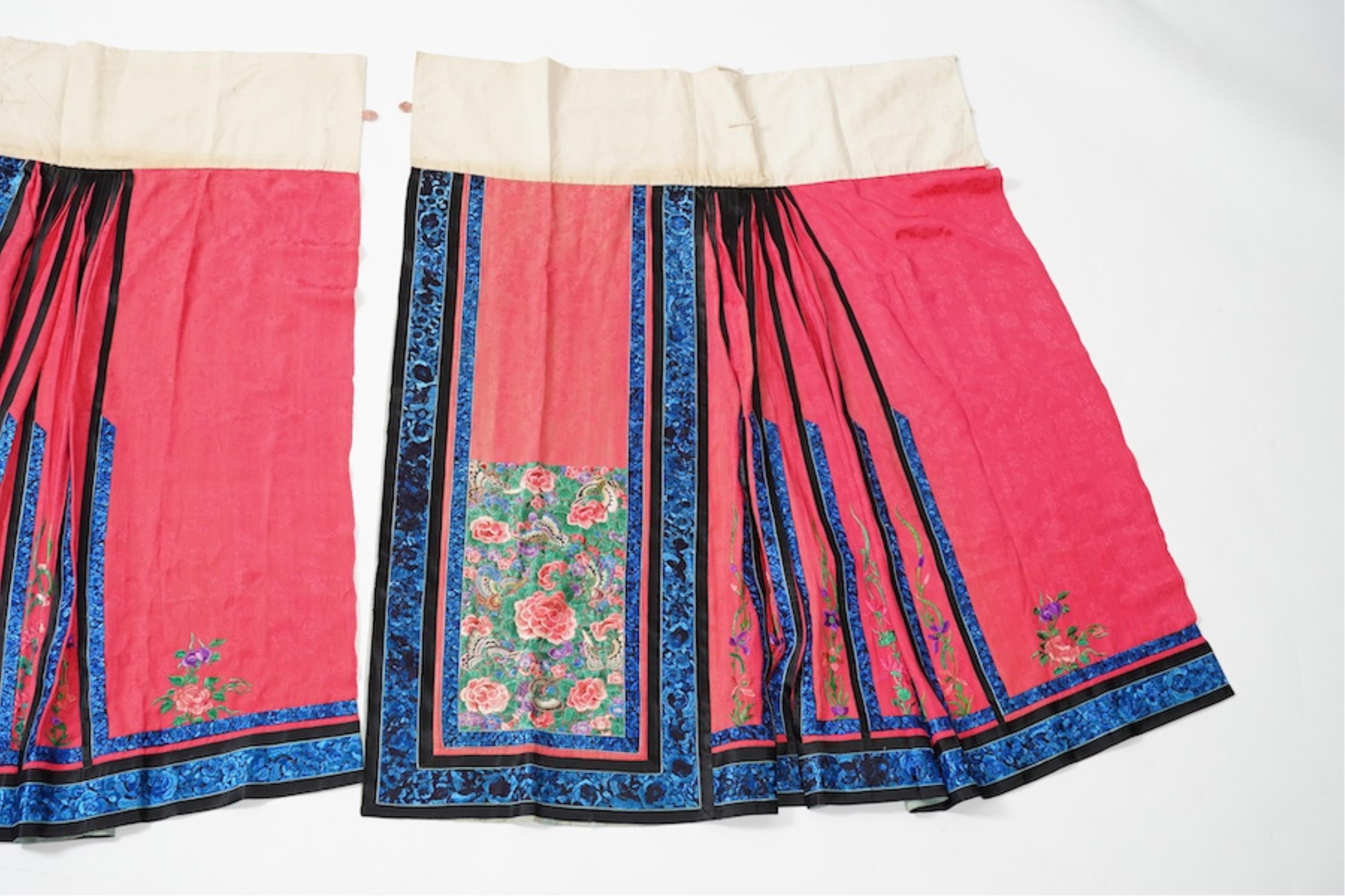 Two late 19th early 20th century Chinese wedding skirts. Made with pink silk damask, embroidered with large decorative silk floral and butterfly front panels bordered by blue embroidered black silk borders between pleats